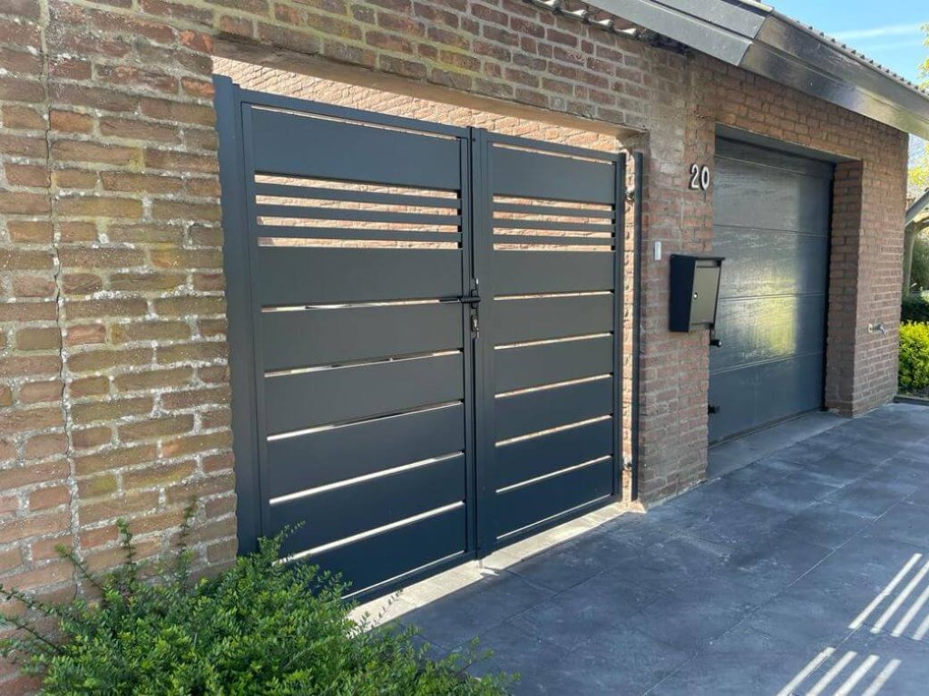 Moderne metalen tuinafsluiting met horizontale lamellen, geplaatst bij een woning met bakstenen gevel