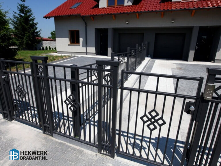 Stijlvol zwart ijzeren hekwerk met decoratieve elementen bij een moderne woning met opritIjzeren hekwerk met decoratief patroon en poort, gemonteerd voor een eigentijdse woning. Duurzaam, onderhoudsarm en geschikt voor opritten of voortuinen.