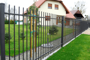 Zwart metalen voortuinhek met verticale spijlen rondom een moderne woning met een rode dakpan en groene tuin