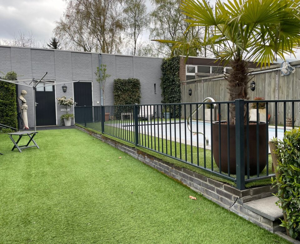 Laag hekwerk rondom groenstrook in stedelijke omgeving met trottoir